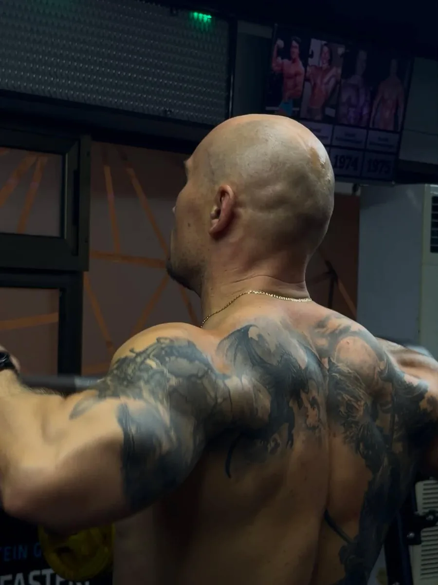 Nikita, back view, pressing overhead in the gym